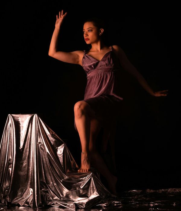 Woman performing light rhythmic movements in a dark studio with teal highlights.
